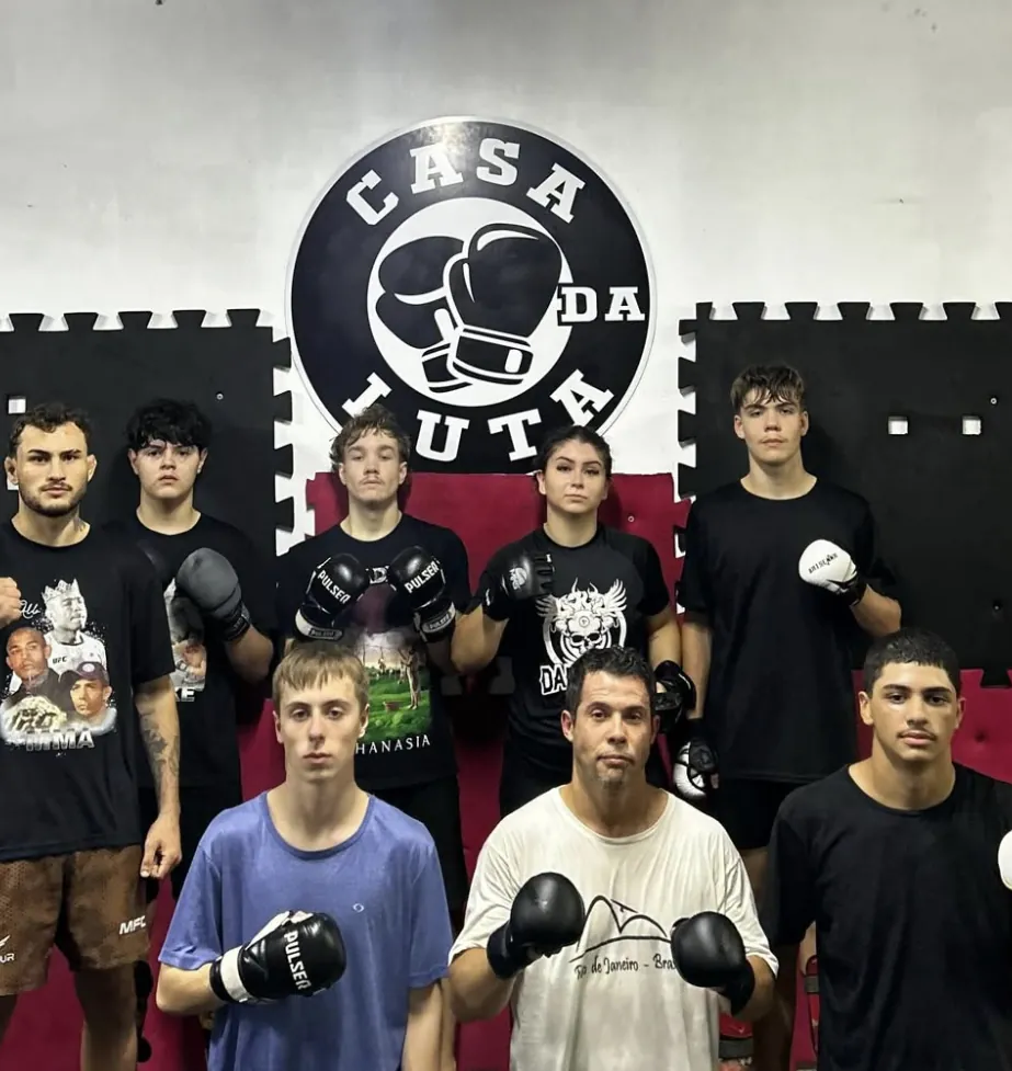 Alunos da Casa da Luta posando com luvas em frente à logo do CT